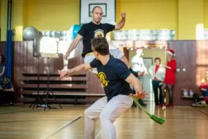 Energetic capoeira performance indoors with audience during daytime.